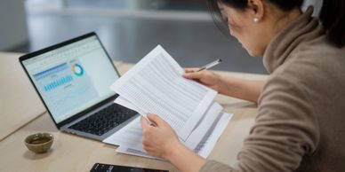 Person analyzing documents with laptop showing graphs nearby.