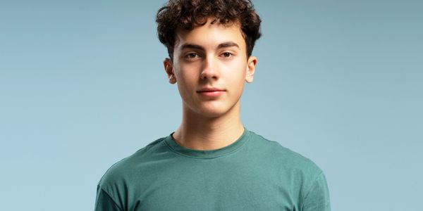 A teenager with curly hair is wearing a green cotton T-shirt and looking into the camera with no exp