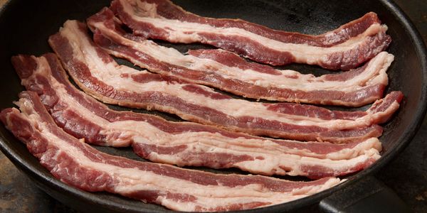 Photo of house smoked bacon from F&D Meats cooking in a cast iron pan. 