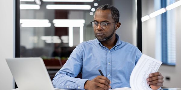 Man analyzing documents at desk with laptop in modern office.