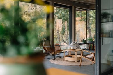 Cozy modern patio with natural wood furniture and large glass windows.