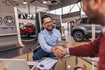 Two men shaking hands in a car dealership, smiling and finalizing a deal.