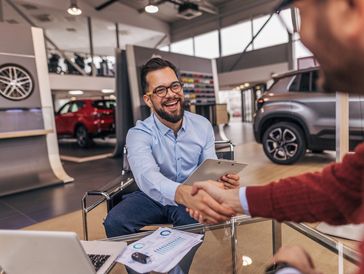 Car salesman shaking hands with a customer in a showroom.