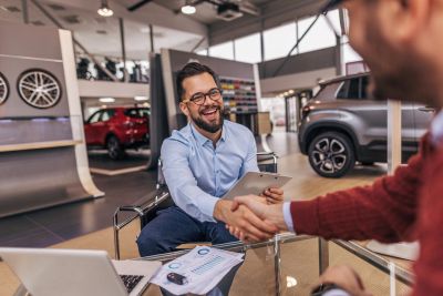 Two men shaking hands in a car dealership.