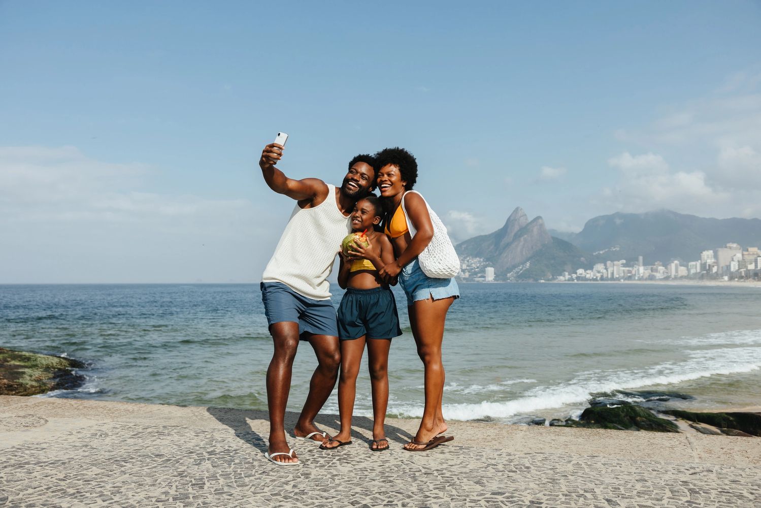 A family taking a selfie at the beach with mountains in the background.