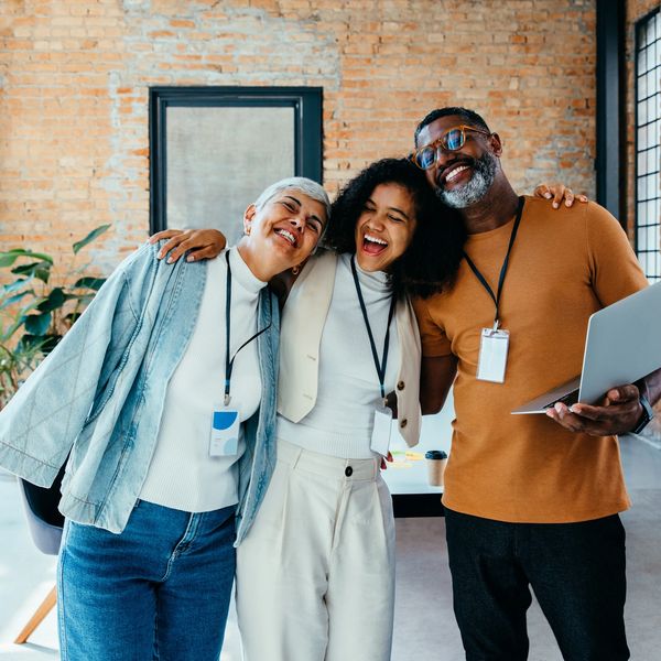 Three colleagues joyfully embracing in a modern office space.