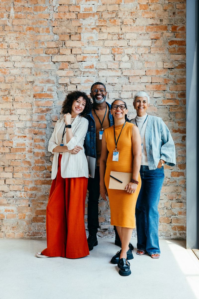 A group of confident, diverse coworkers standing together against a rustic brick wall in a modern office setting, showcasing teamwork and camaraderie.