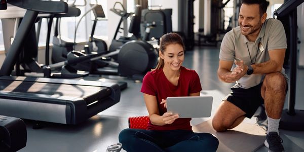 Woman and trainer reviewing workout plan on tablet in gym.