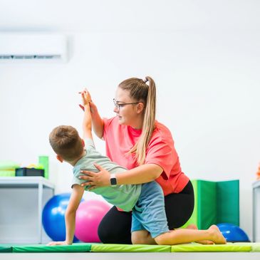Therapist helping child with exercise in bright room.