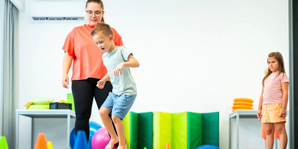 Child balancing on a yellow rock with adult supervision.