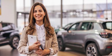 Smiling woman in a car dealership holding a tablet and car keys.