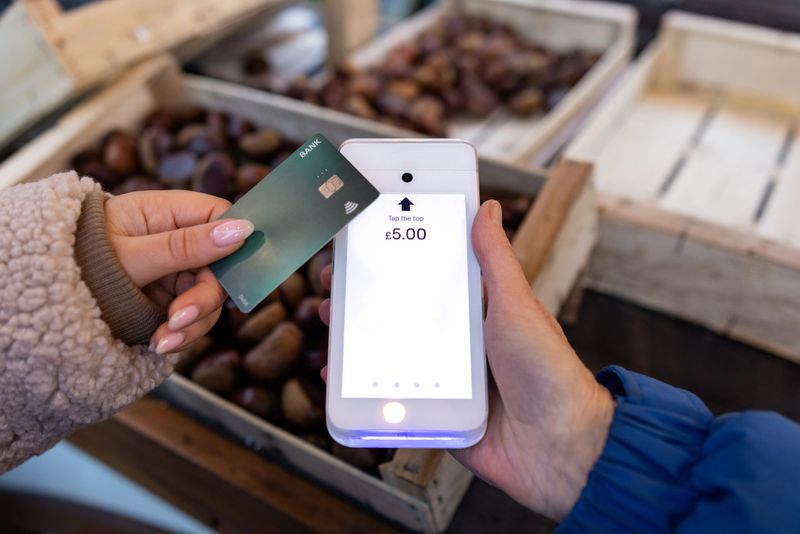 A close-up point of view of an unrecognisable young woman at the Christmas markets in Newcastle, England. She is at a market stall selling roasted chestnuts and she is making a contactless payment using a debit card on a card reader.