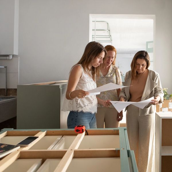 Three women examining papers in a room under renovation.