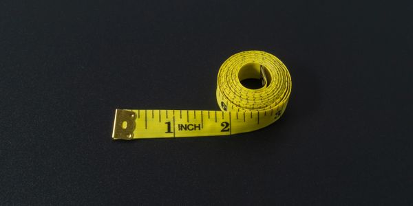 Yellow measuring tape rolled up on a dark surface.