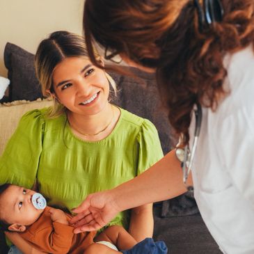 A smiling mother holding her baby while talking to a healthcare professional.