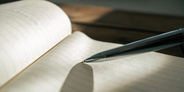 A pen resting on an open lined notebook with sunlight casting shadows.