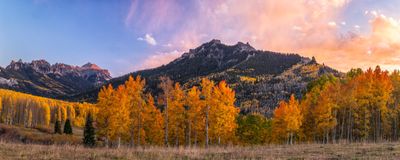 Mountains with fall foliage under a vibrant sky at sunset.