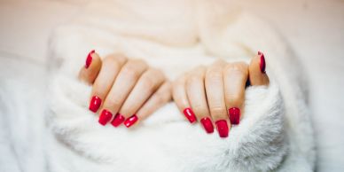 Hands with red manicured nails wrapped in a white fuzzy blanket.