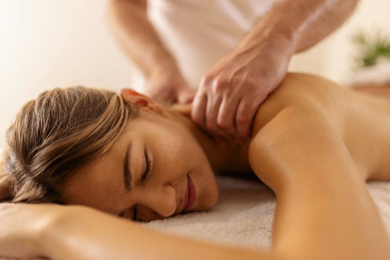 Beautiful woman is lying on stomach on a massage table in a salon, and a masseur is massaging her back. Her eyes are closed, she is enjoying.