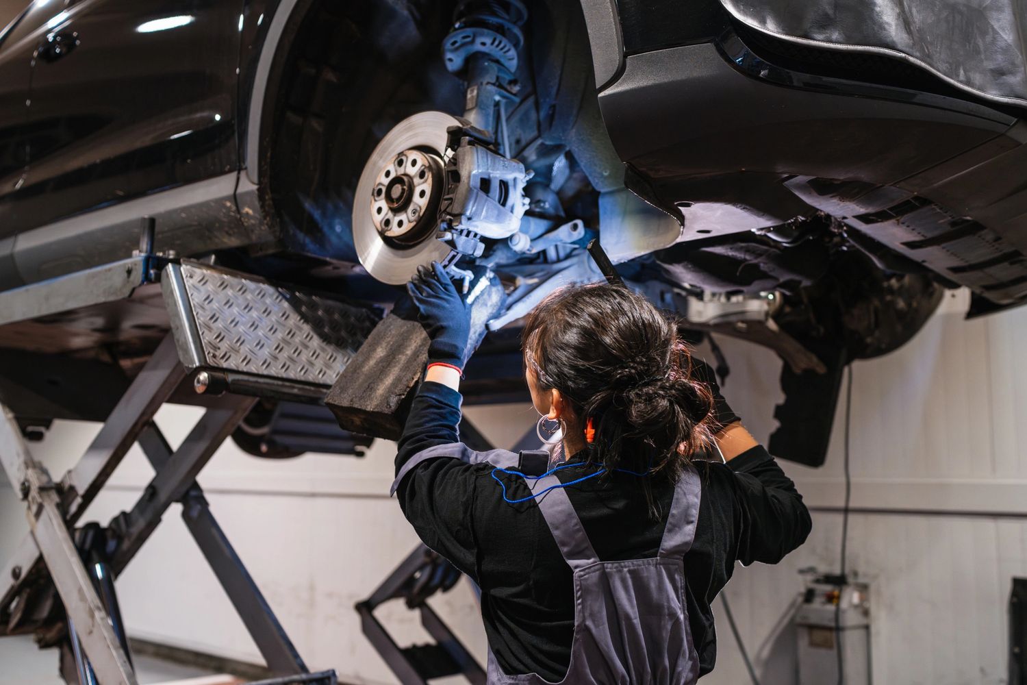 A mechanic inspects a car's brake system on a lift in a workshop.