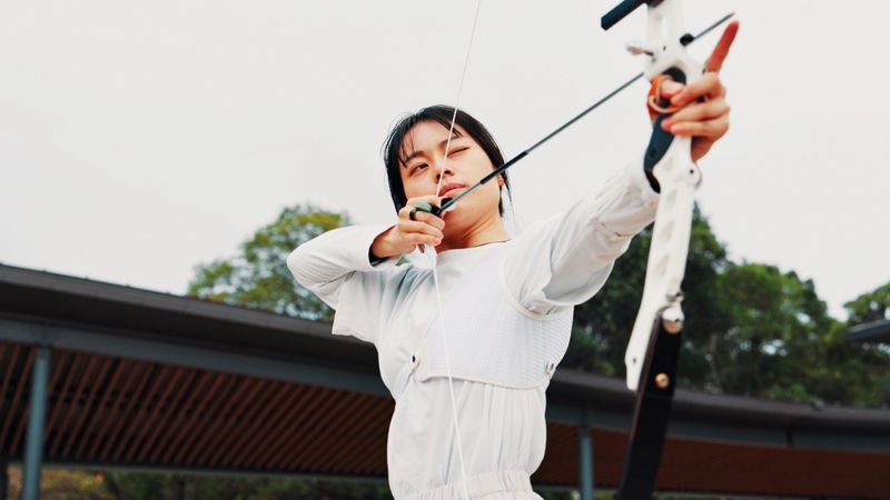 Serious, training and woman with bow, aim and preparing for competition, equipment or outdoor for game. Contest, athlete and practice from tournament, skills and challenge for person