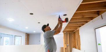 Man using a power drill to install ceiling panels in a room under renovation.