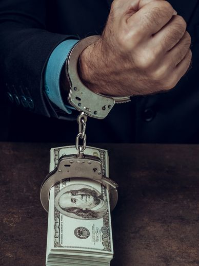 Man in handcuffs chained to a stack of hundred-dollar bills.