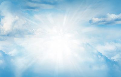 Bright sun rays shining through fluffy clouds in a clear blue sky.