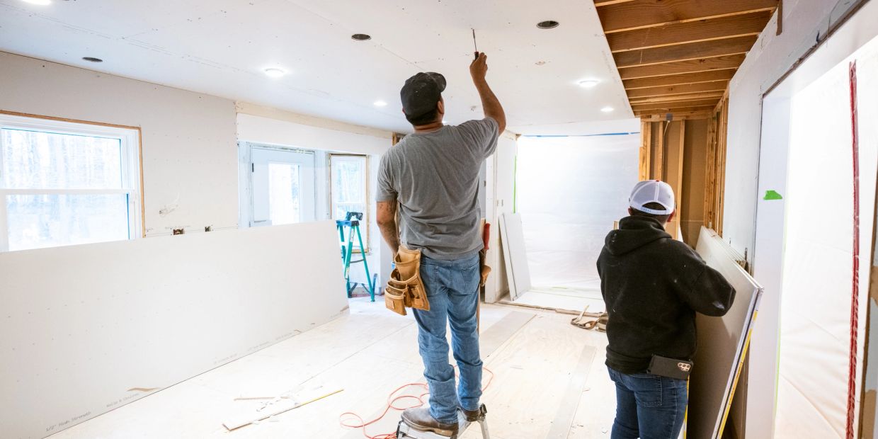Two workers installing drywall in a room under construction.