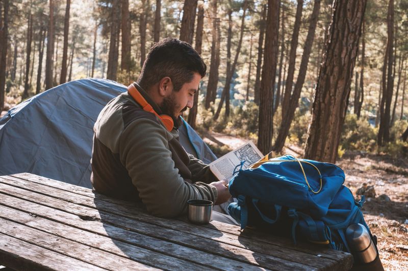 A hiker has set up camp in the forest and is reading a book.