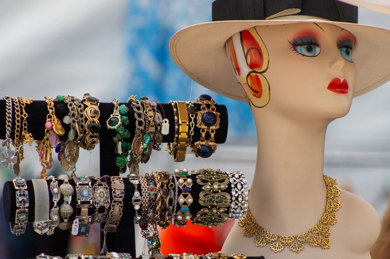A fabulous vintage retro art deco style mannequin wears a hat and is displayed next to a collection of vintage and antique bracelets of multiple styles.