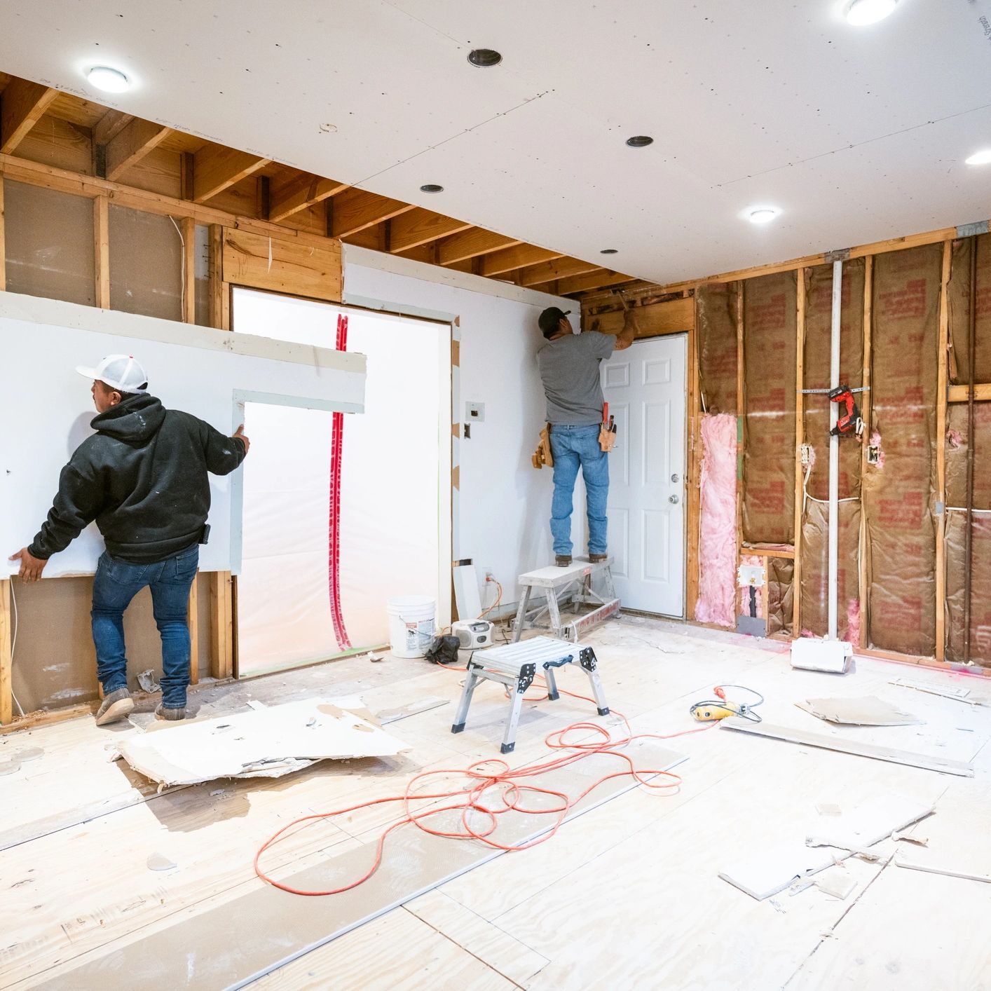 Two workers installing drywall in a room under renovation.