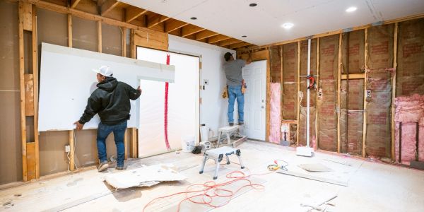 Two workers installing drywall in a room under renovation.
