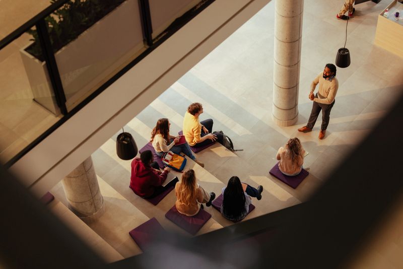 High angle view of a teacher giving a lesson to students sitting on cushions in a modern university building