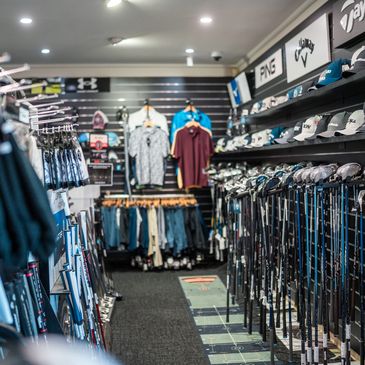 Golf store aisle showcasing clubs, hats, and apparel.