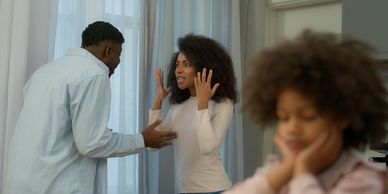 A couple arguing indoors with a child distressed in the foreground.