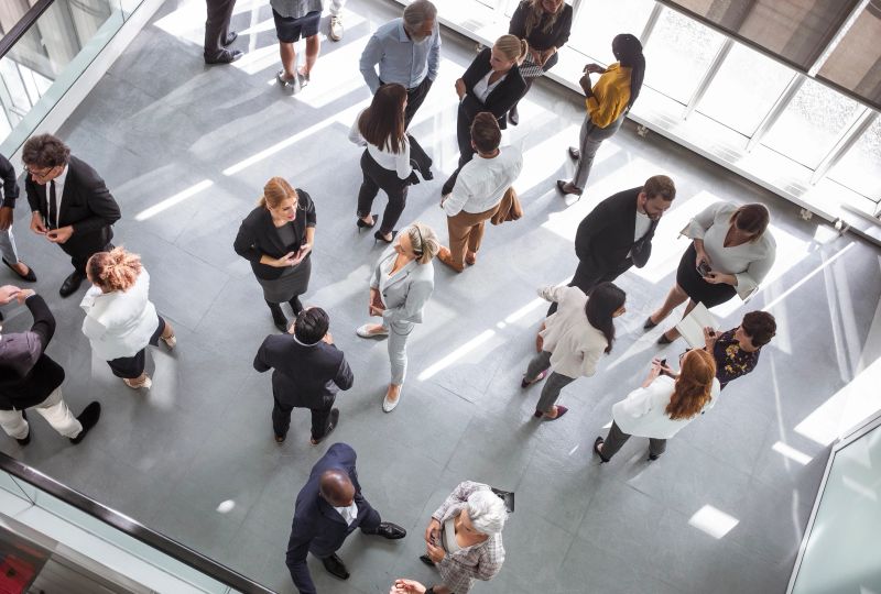 Diverse business professionals engaging at a conference event, dressed in formal business attire, networking and discussing ideas. Set in a modern conference hall, attendees use laptops and notepads for effective communication and collaboration.