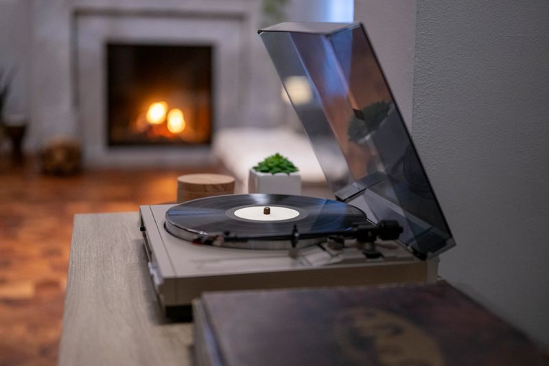 A turntable playing a vinyl record is set on a wooden surface, with a glowing fireplace in the background creating a warm, nostalgic ambiance.