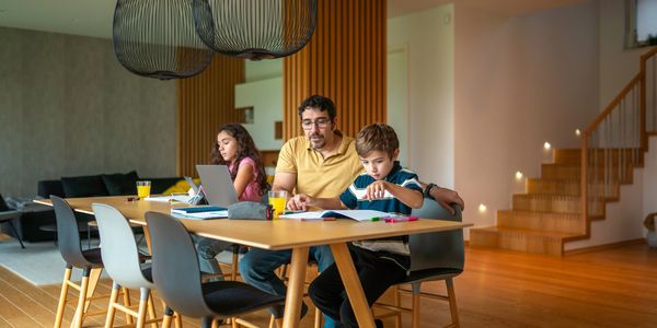 Father helping children with homework at dining table.
