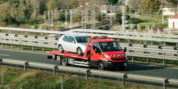 Red tow truck carrying a silver car on a highway.