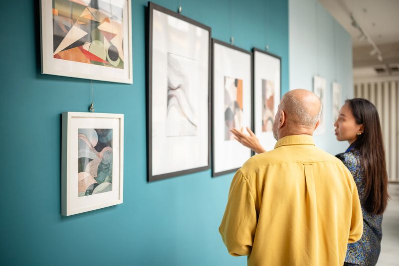 Curator with a visitor viewing abstract paintings in a modern art gallery. The scene showcases appreciation for creativity and design, emphasizing cultural connection and appreciation of visual arts in a museum-like setting.