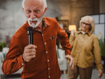 Elderly man singing with a microphone and woman dancing.