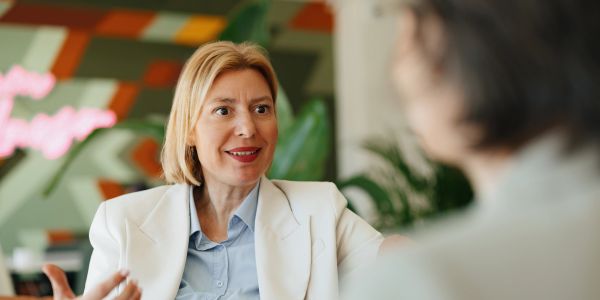 Woman in white blazer speaking to another person.