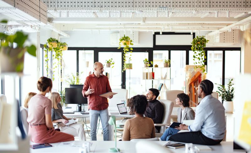 A team collaborates in a modern co-working space filled with plants and natural light, working on a project with focus and engagement. The environment fosters creativity and teamwork.