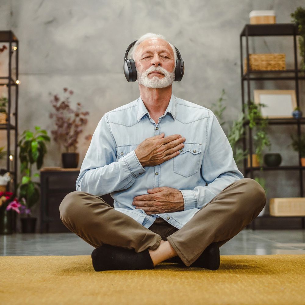 Elderly man meditating with headphones, hands on chest and stomach.