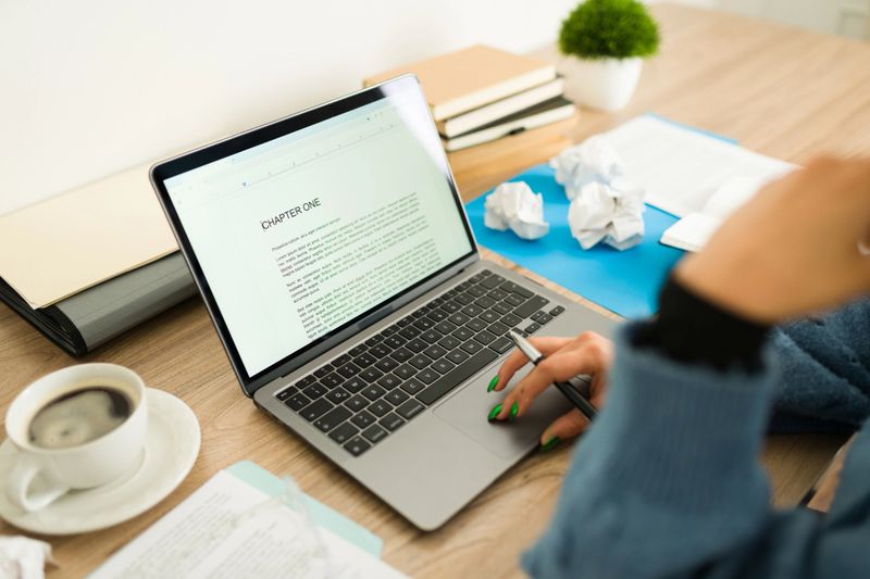 Closeup of a young woman author writing chapter one of her new book using a laptop, taking a break from work and having a cup of coffee