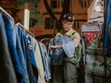 A man examines a denim jacket at a nighttime outdoor market booth.