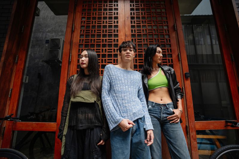 Three fashionable friends stand confidently in front of a decorative wooden door, each showcasing their unique style and attitude.