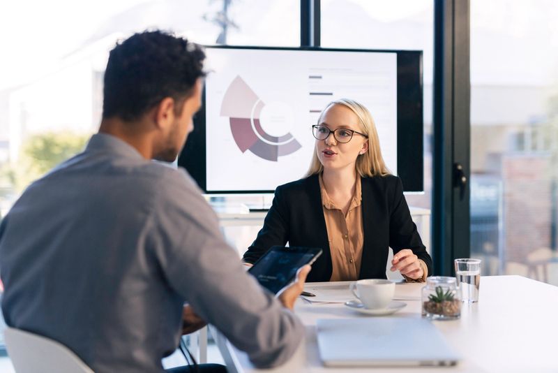Two professionals engage in a focused business meeting in a modern office environment. They discuss data displayed on a screen, highlighting teamwork and effective communication. The scene conveys professionalism, collaboration, and a dynamic workplace atmosphere.