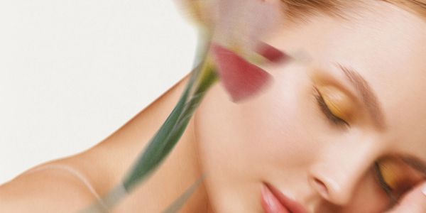 Close-up of a woman with soft makeup and a blurred flower in the foreground.